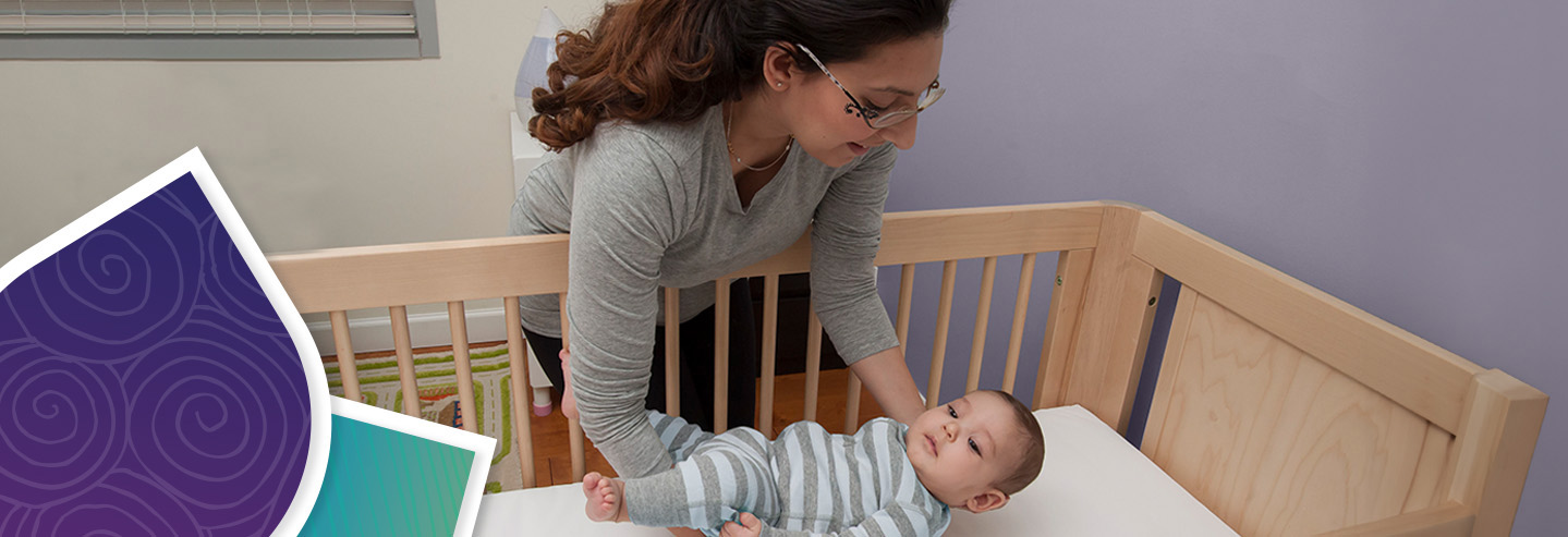 An adult laying down an infant in a crib on its back.