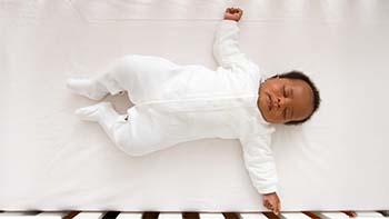 Baby sleeping alone on their back in a crib with no items around them.